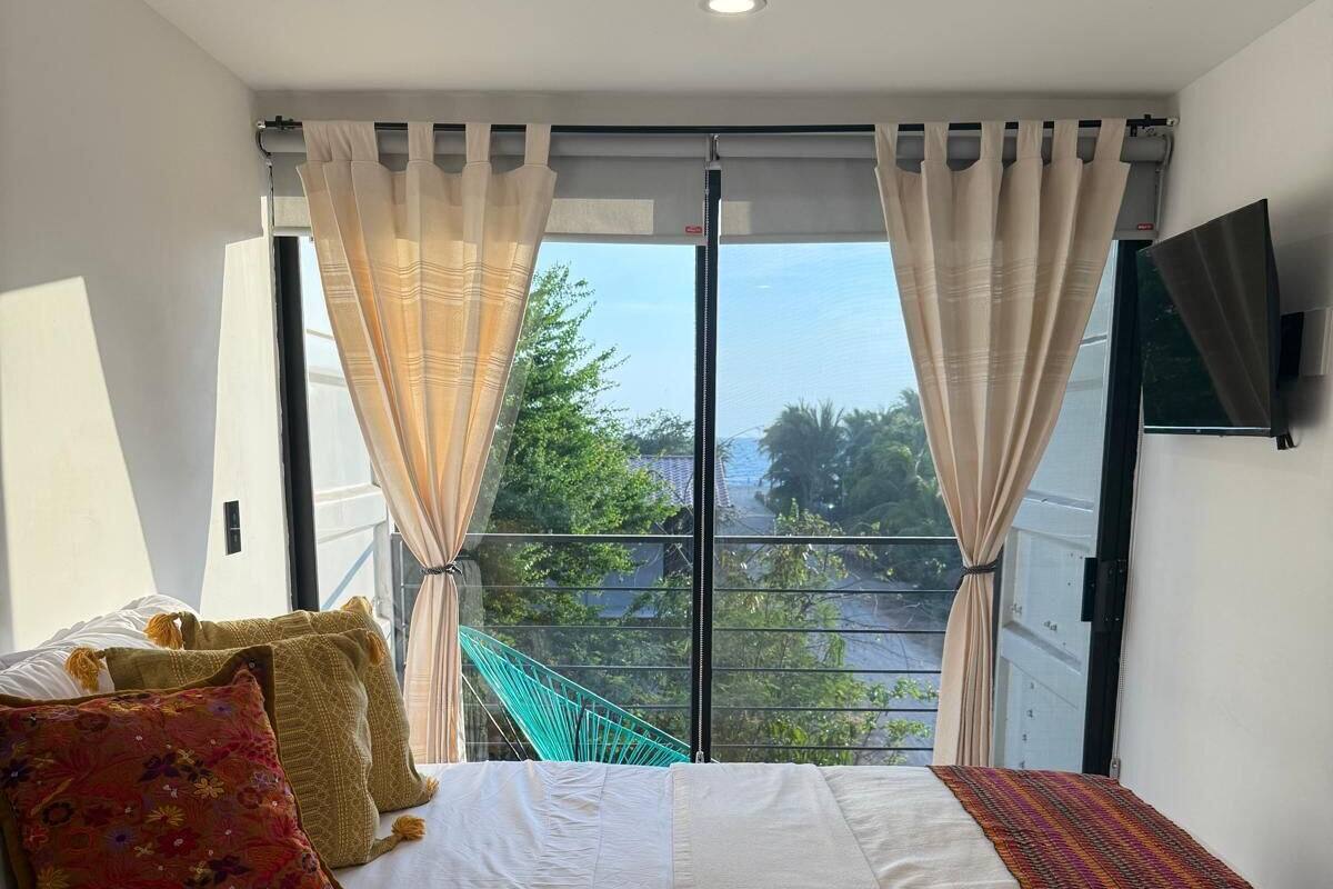 Une chambre à coucher avec un lit, des rideaux, une télévision et une vue sur la verdure à l’extérieur.