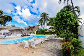 A swimming pool area with lounge chairs and umbrellas, surrounded by palm trees and a clear sky. - Pousada Recanto do Aconchego (Ipojuca)