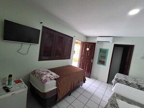 A bedroom with a single bed, a bedside table, a TV mounted on the wall, a wardrobe, and a door leading to another room. - Pousada Recanto do Aconchego (Ipojuca)