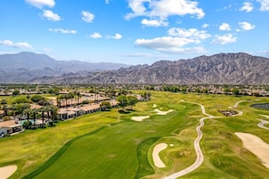 Un parcours de golf avec une chaîne de montagnes en arrière-plan, entouré d’immeubles résidentiels et de palmiers.