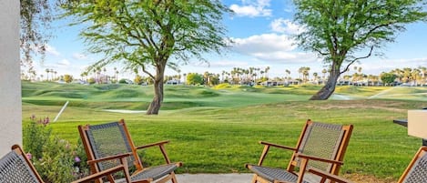 A patio with two wooden chairs facing a golf course.