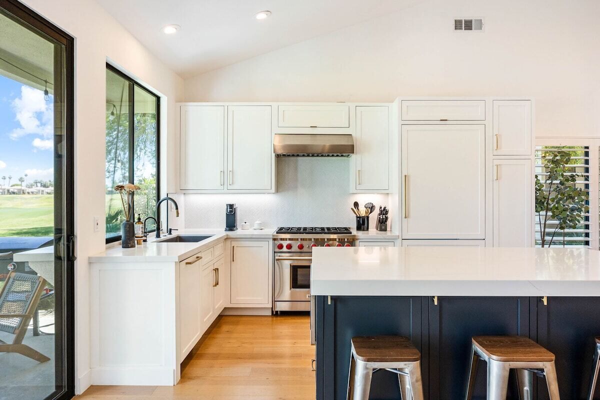 A modern kitchen with white cabinets, a central island, and a view of the outdoors.