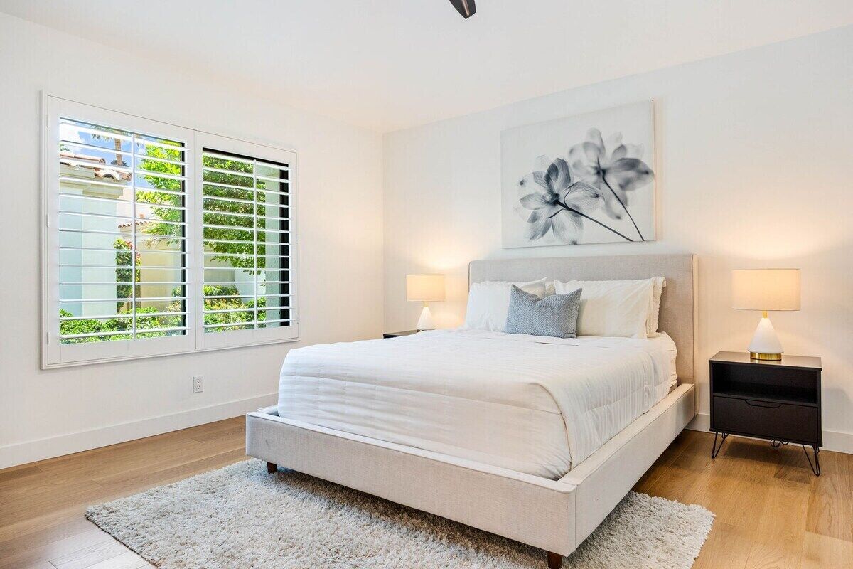 Een slaapkamer met een groot bed, twee nachtkastjes, een raam met zonwering en een kunstwerk aan de muur.