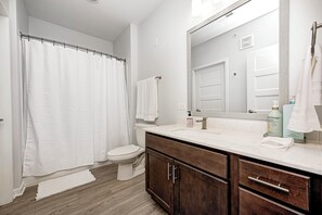 Un baño moderno con cortina de ducha, inodoro, tocador con espejo y lavamanos.