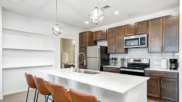 A modern kitchen with a large island, brown cabinets, stainless steel appliances, and pendant lighting. - Comfy Cozy - 2King bed/2bth Fishers (Fishers)