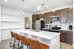 Una cocina moderna con una isla grande, armarios marrones, electrodomésticos de acero inoxidable e iluminación colgante.