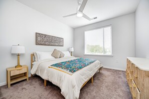 Un dormitorio con una cama, mesitas de noche, ventilador de techo, ventana con persianas y cómoda.