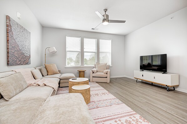 Una sala de estar moderna con un sofá, un sillón, un televisor y un ventilador de techo.