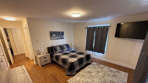 A bedroom with a bed, nightstands, a TV, and a window with curtains.