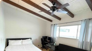 A bedroom with a bed, a desk, a black sofa, and a ceiling fan.