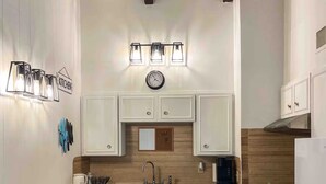 A modern kitchen with white cabinets, a wooden countertop, a sink, a stove, and a clock on the wall.