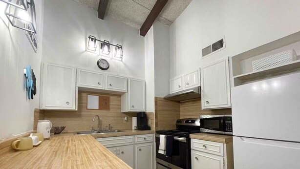 A modern kitchen with white cabinets, a wooden countertop, a stove, a microwave, and a refrigerator.