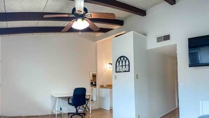 A spacious room with a wooden floor, a ceiling fan, a desk with a chair, and a bed.