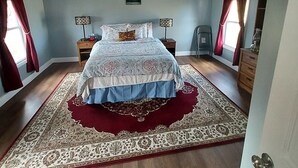 Ein Schlafzimmer mit einem Bett, einem Deckenventilator, einem Nachttisch, einer Kommode und einem Fenster mit Vorhängen.