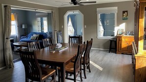 Ein Essbereich mit Holztisch und -stühlen, einem Deckenventilator und Blick auf ein Wohnzimmer mit Sofa und Vorhängen.