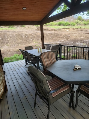 A covered outdoor seating area with a table and chairs, a wooden deck, and a view of a landscaped area. - Newly renovated 5 bedroom pet friendly house in Keuka NY. First floor ensuite (Keuka Park)