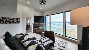 A modern bedroom with a large bed, a TV, and a view of a bridge. - Spectacular Bridge and Bay Views! Bayfront, Hot Tub, Dog Friendly, Fireplace! (Waldport)