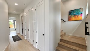 A hallway with white doors, a wooden staircase, and a colorful abstract painting on the wall. - Spectacular Bridge and Bay Views! Bayfront, Hot Tub, Dog Friendly, Fireplace! (Waldport)