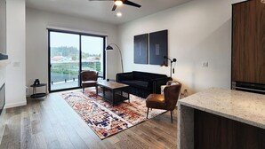A modern living room with a large sliding glass door leading to a balcony, a dark-colored sofa, a coffee table, and a rug. - Hot Tub! Dog Friendly! Short Walk to Sandy Beach! (Waldport)
