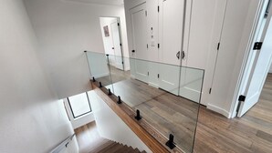 A staircase with glass railings leading to a landing with white cabinets and a door. - Hot Tub! Dog Friendly! Short Walk to Sandy Beach! (Waldport)