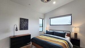 A modern bedroom with a bed, bedside lamps, a radiator, and a large window with a view. - Hot Tub! Dog Friendly! Short Walk to Sandy Beach! (Waldport)