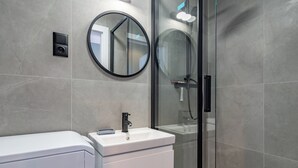 A modern bathroom with a glass-enclosed shower, a white sink, and a round mirror.