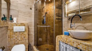 Une salle de bain avec une douche à parois de verre, des toilettes blanches, un lavabo avec un grand bac et un mur recouvert de carreaux.