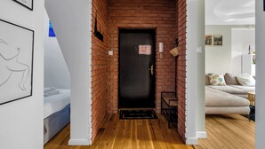 Un couloir avec une porte noire, un plancher en bois et un mur en briques.