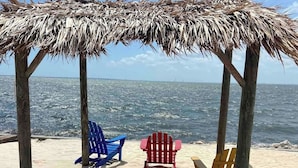 Una playa con una estructura de techo de paja y tres sillas.