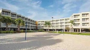 Un hotel con varios pisos, un patio de arena y palmeras.