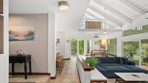 A spacious living area with a large sofa, a dining table, and a kitchen area with a view of the outdoors. - 2br 2ba Modern Kamahana, Pool, Close to Beach (Princeville)