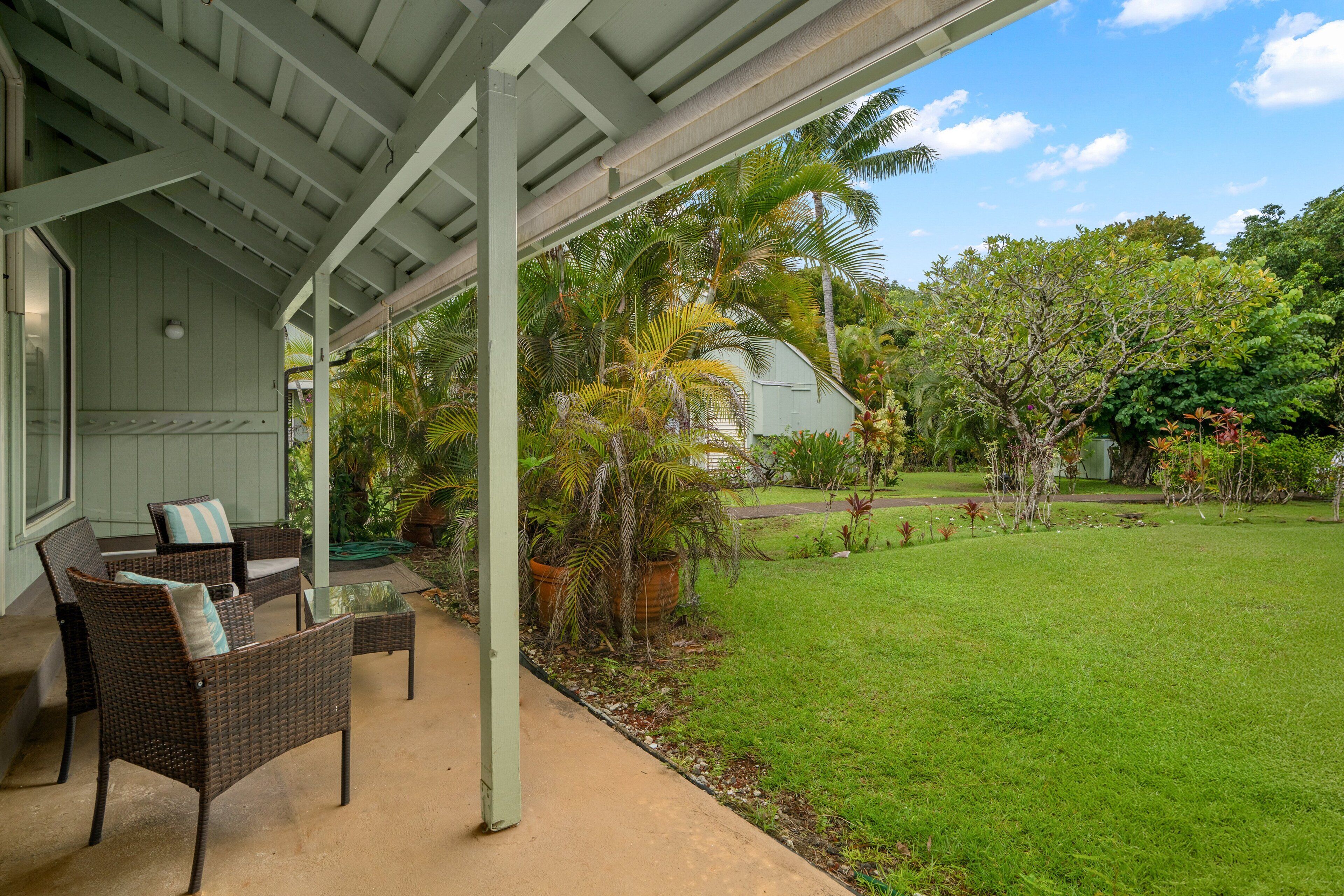 A covered patio with wicker furniture and a view of a lush garden.
