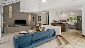 A modern living room with a blue sofa, a flat-screen TV, and a ceiling fan. - 2br 2ba Modern Kamahana, Pool, Close to Beach (Princeville)