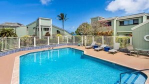 A swimming pool with lounge chairs and a white fence. - Cozy Modern Kamahana Studio, Pool, WiFi (Princeville)