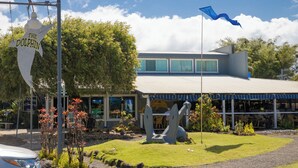 A building with a covered outdoor seating area, a dolphin sculpture, and a flag. - Cozy Modern Kamahana Studio, Pool, WiFi (Princeville)