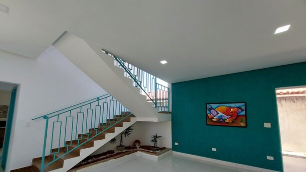 A modern interior with a staircase, a teal accent wall, and a colorful abstract painting. - Recanto Ingles (Caraguatatuba)
