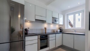 A modern kitchen with stainless steel appliances, white cabinetry, and a large window providing natural light.