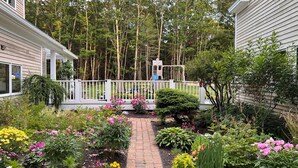 A garden with a brick pathway, various plants, and a white fence. - Cozy Freeport Bungalow (Freeport)