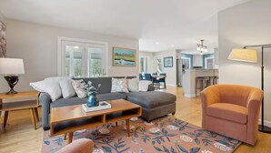 A modern living room with a grey sofa, a wooden coffee table, and a patterned rug. There is a dining area in the background with a table and chairs. - Cozy Freeport Bungalow (Freeport)