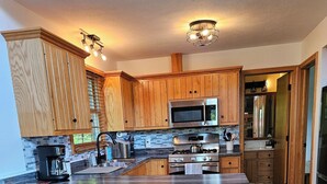 A modern kitchen with wooden cabinets, a large island with bar stools, stainless steel appliances, and a backsplash with a mosaic tile pattern. -  Springhaven Oasis Cabin (Newcomerstown)