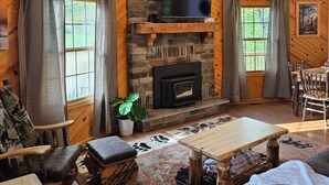 A log cabin interior with a stone fireplace, mounted deer heads, a television, and a dining area. -  Springhaven Oasis Cabin (Newcomerstown)