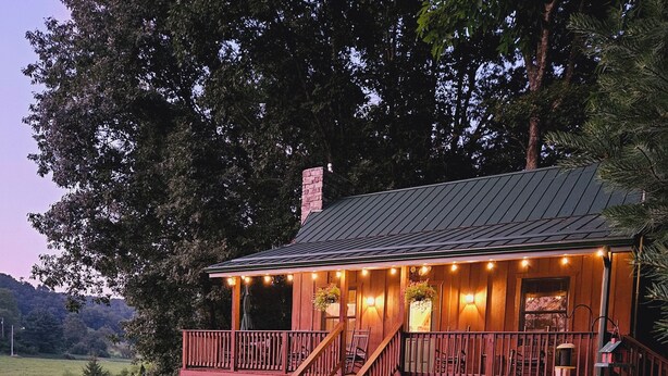 A wooden cabin with a porch, a staircase, and a pond in the background. -  Springhaven Oasis Cabin (Newcomerstown)