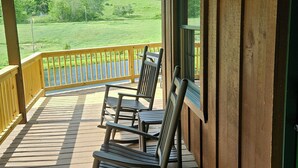 A wooden deck with rocking chairs and a view of a green landscape. -  Springhaven Oasis Cabin (Newcomerstown)