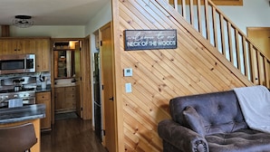 A wooden staircase leading to a loft area, a kitchen with modern appliances, and a leather sofa in a cozy living space. -  Springhaven Oasis Cabin (Newcomerstown)