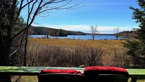 A view from a deck overlooking a lake with a grassy field and trees in the background.