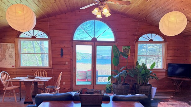 A cozy cabin interior with wooden walls, a dining area with a table and chairs, a sofa, and a TV.