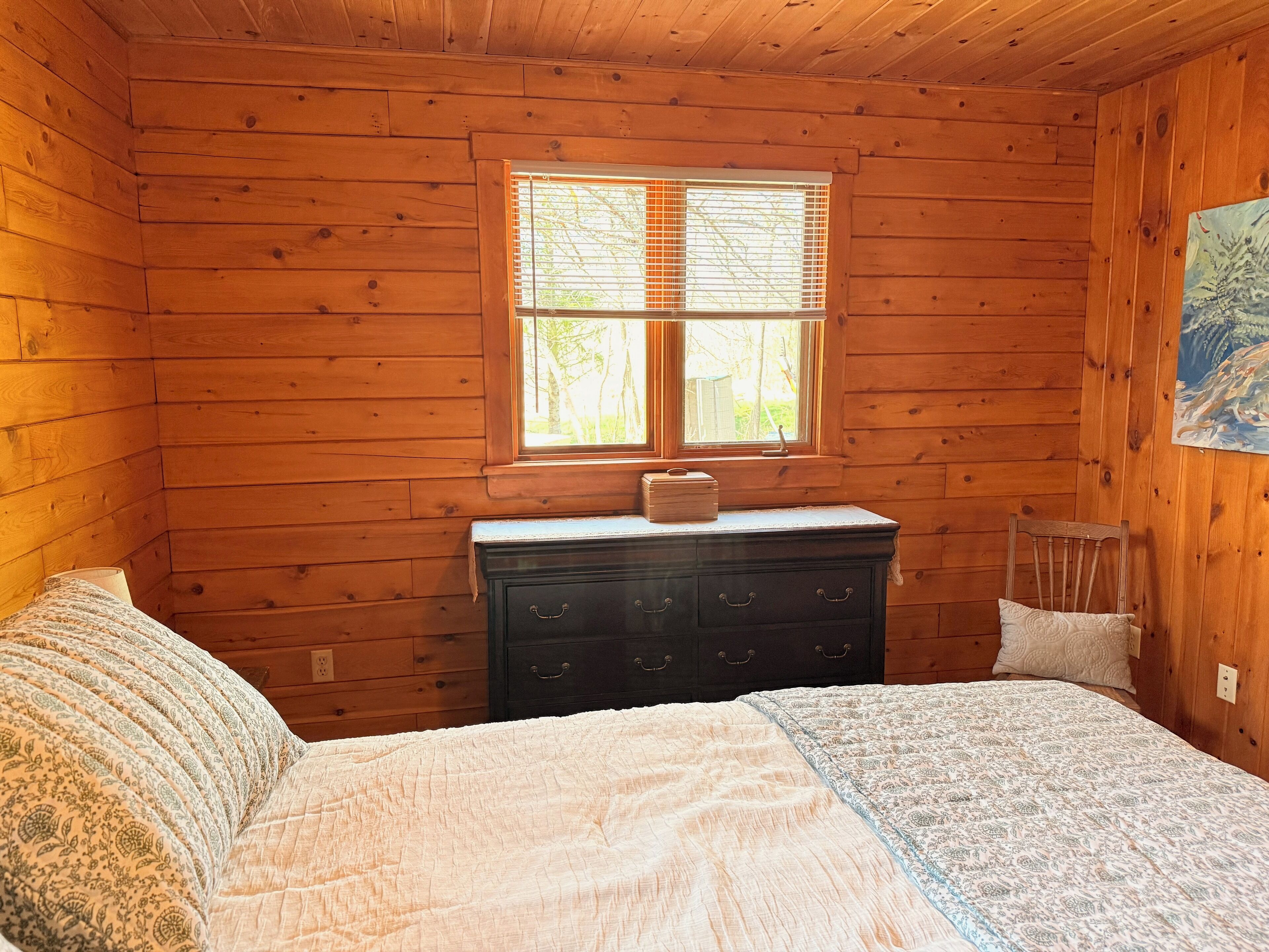 A wooden cabin bedroom with a bed, dresser, and window.
