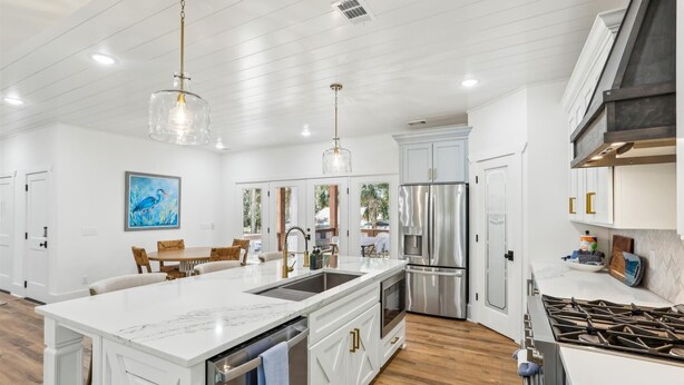 A modern kitchen with a large island, stainless steel appliances, and a dining area with a view to the outdoors. - 4 Elderberry Ln, New Build, Elevator, Steps to Beach, Putting Green, Private Pool (Hilton Head Island)