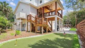 A two-story house with a wooden deck and a small patio area. - 4 Elderberry Ln, New Build, Elevator, Steps to Beach, Putting Green, Private Pool (Hilton Head Island)