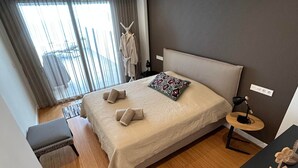 Une chambre d’hôtel moderne avec un grand lit, une table de chevet, une petite table ronde et une vue sur l’extérieur.